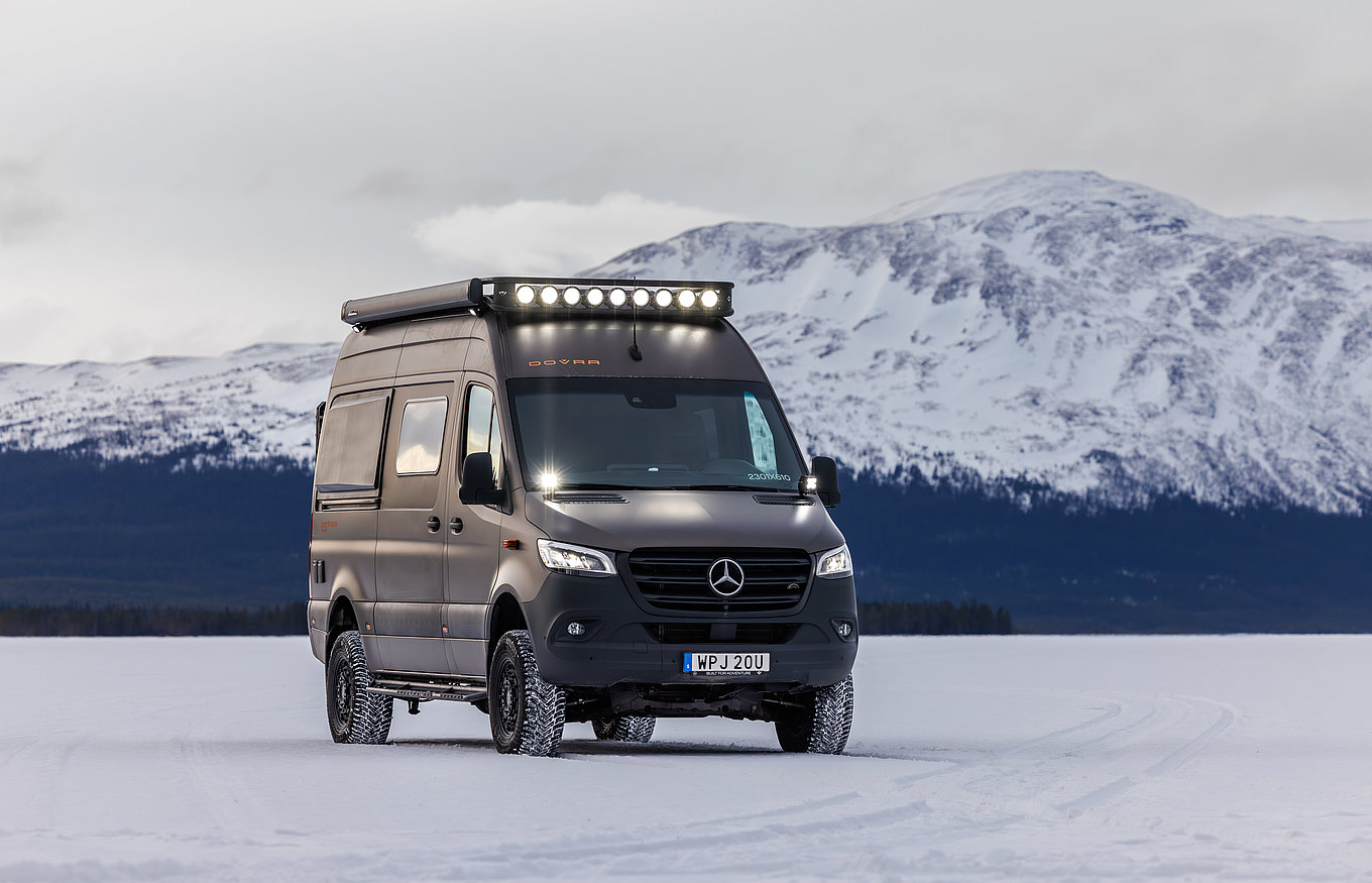 Ein Camper Van von Dovra fährt durch eine Schneelandschaft. 